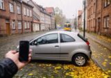 Zaparkowany samochód na brukowanej ulicy we Wrocławiu i dłoń z telefonem przy błotniku